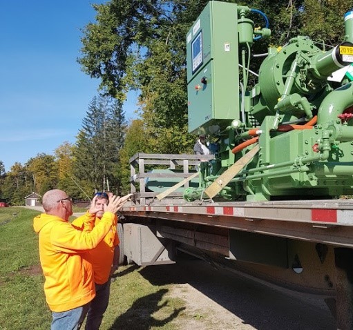 Picture of the General Manager and Head of Operations look up at a large metal compressor on a flat bed truck.